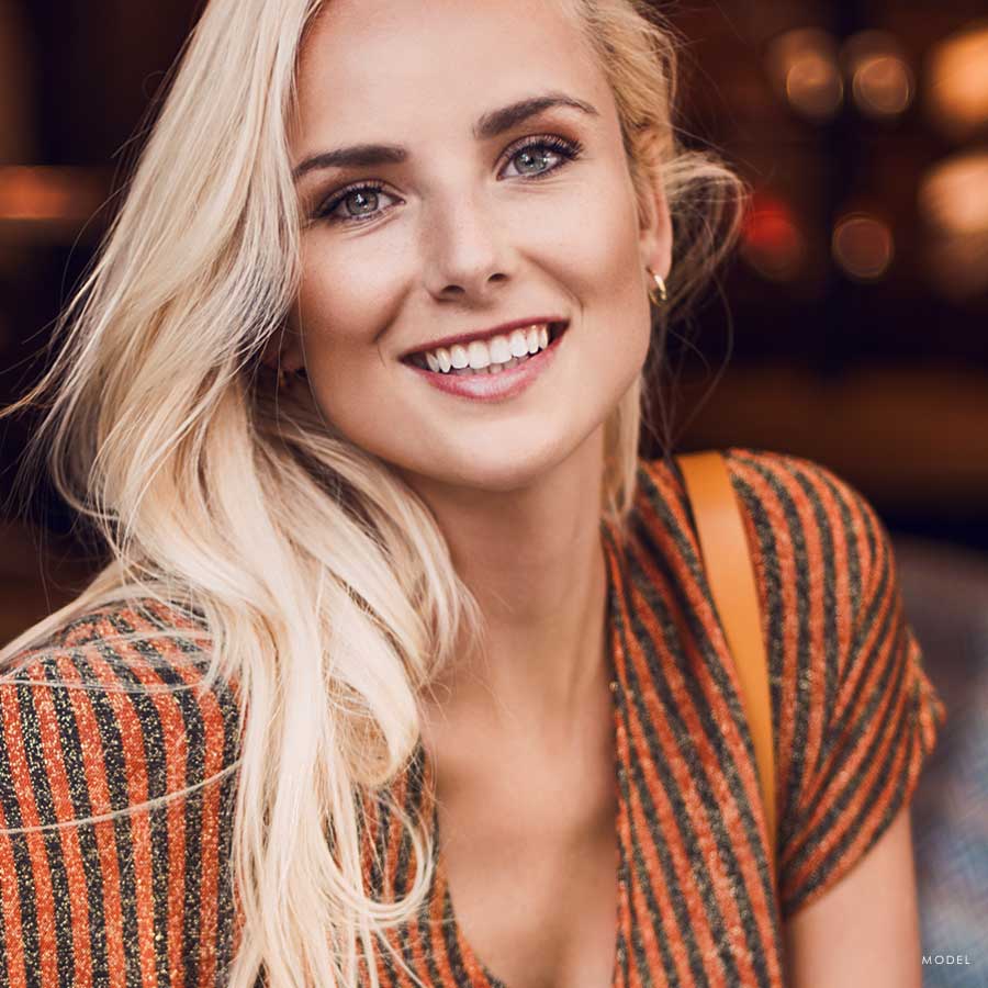 Headshot of a happy blonde woman wearing an orange striped blouse