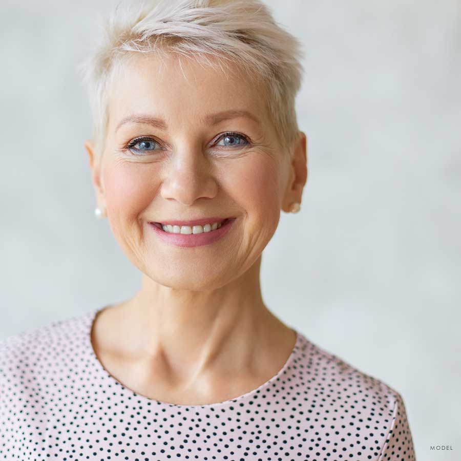 Headshot of a older woman smiling and wearing earrings and pink polkadot blouse