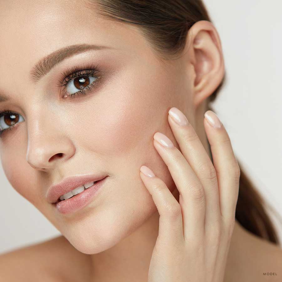 Headshot of a young woman examining her cheeks