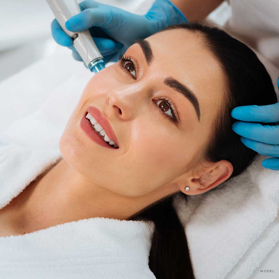 Headshot of a woman laying in a spa bed and getting a facial treatment applied to her cheek