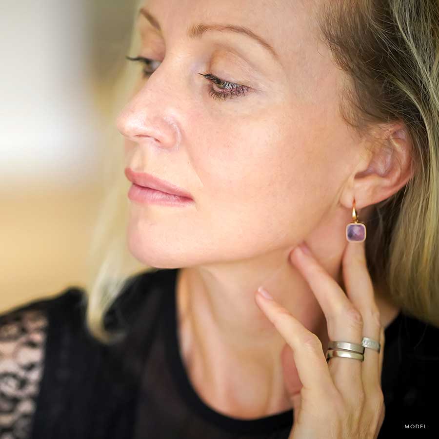 Sideview headshot of a middle aged woman wearing jewelry and caressing her neck