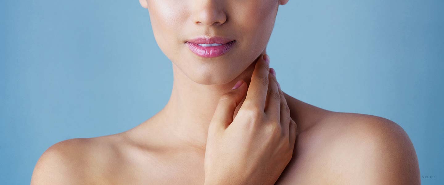 Close up of a woman's bare shoulders and lower face with pink lipstick and hand caressing the neck