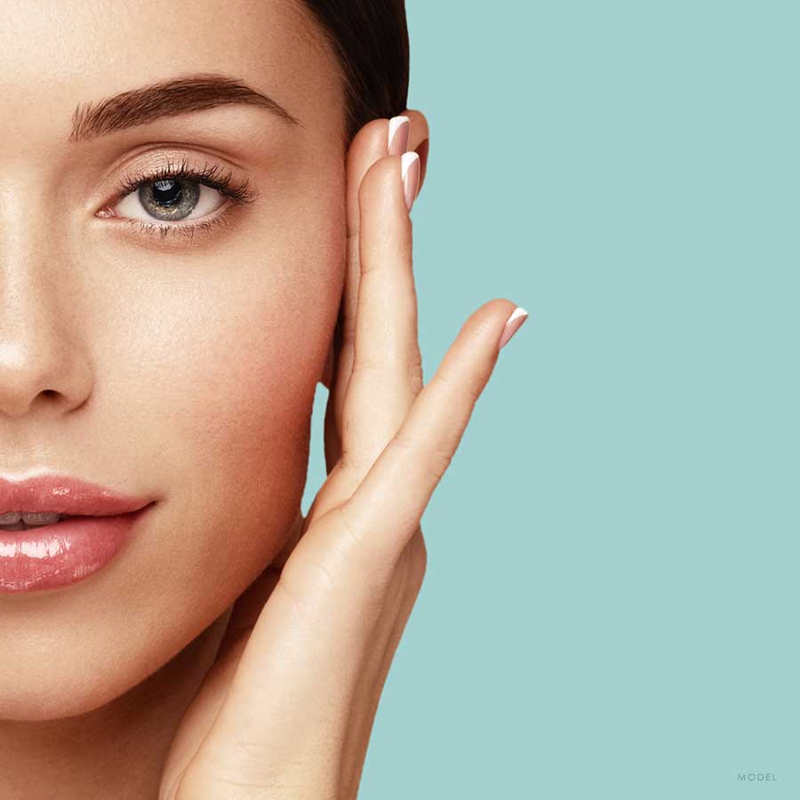 Headshot of half of a female model model's clear face with her fingers brushing her face