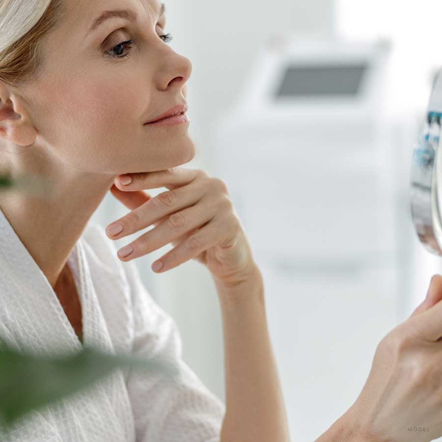 A middle aged woman examining her face with a mirror